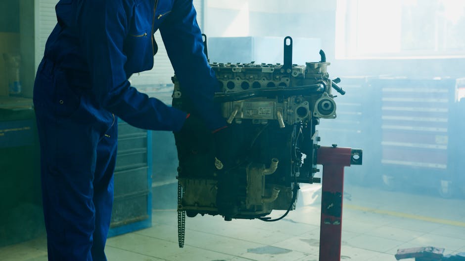Mechanic in blue overalls inspecting an engine in an indoor garage