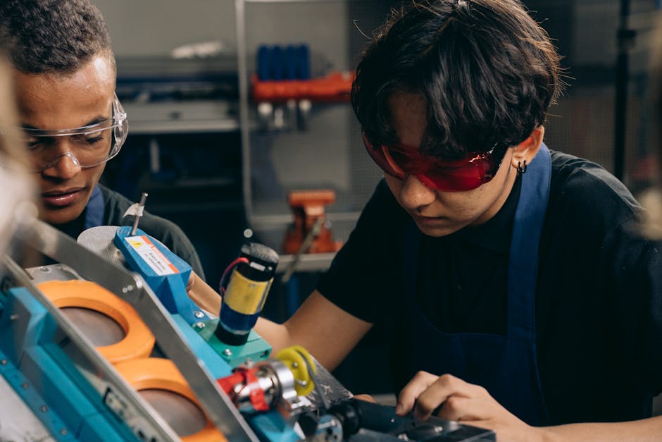 Two young engineers concentrating on precision work in a technical workshop, wearing safety goggles